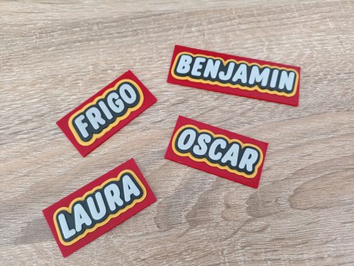Magnet style LEGO© Étiquettes de noms : Frigo, Benjamin, Oscar, Laura sur un fond en bois.