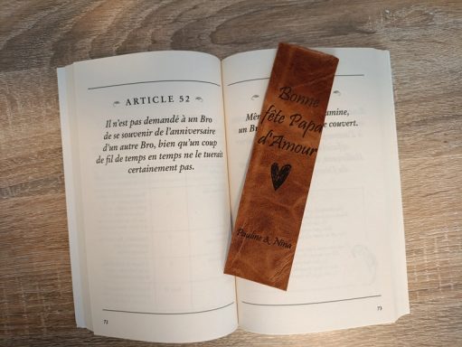 Marque-page Cuir Gravé Personnalisé Marque-page en bois sur un livre ouvert, texte sur une des pages.