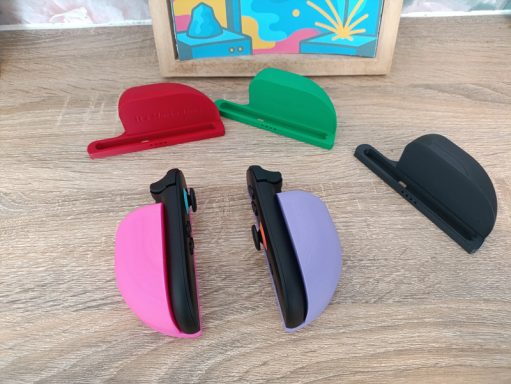 Support souris Switch2 Quatre clips de couleur (rouge, vert, noir, rose, violet) posés sur une surface en bois.